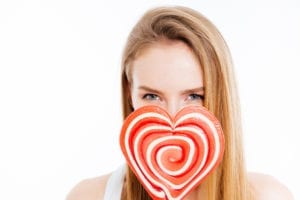 cute lovely young woman covered face with heatr shaped lollipop over white background SY8Nvk0Si