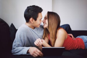 romantic teenage couple on couch looking at each other with digital tablet young couple in lover about to kiss each other on sofa at home mixed race man and woman with tablet pc indoors SaeGczINKe