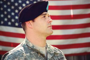 man wearing combat hat and top looking up near flag of america