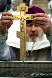 adult priest dipping christian cross in water