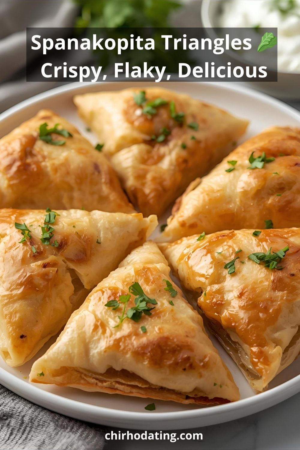 Flaky golden spanakopita triangles on a plate with dip.